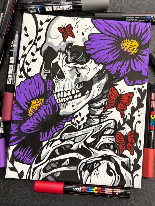 Coloring book with skeleton and flowers design, surrounded by markers on a dark surface.